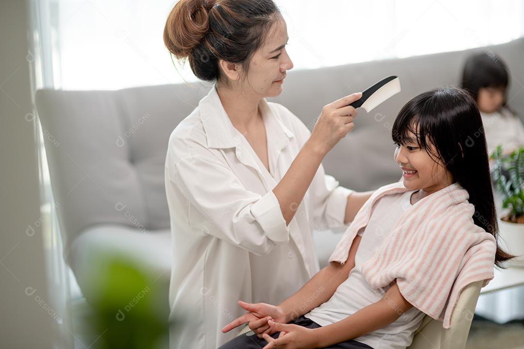 Jovem mãe asiática amarrando o cabelo da filha