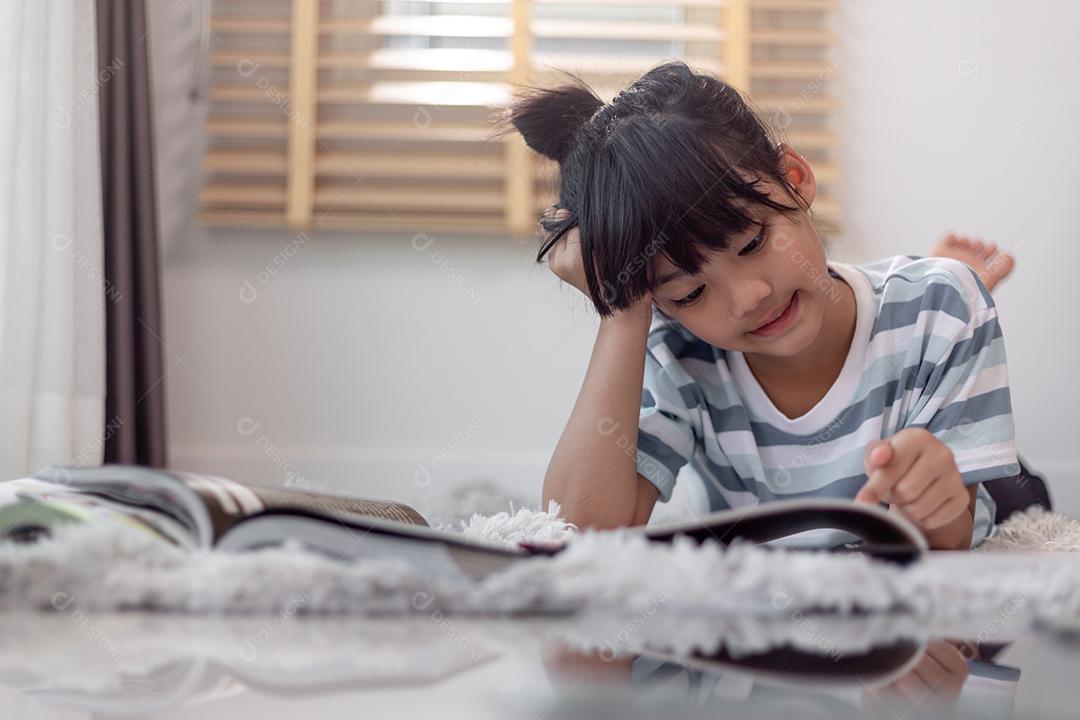 Livro de leitura infantil em casa. Menina deitada e lendo dentro de casa