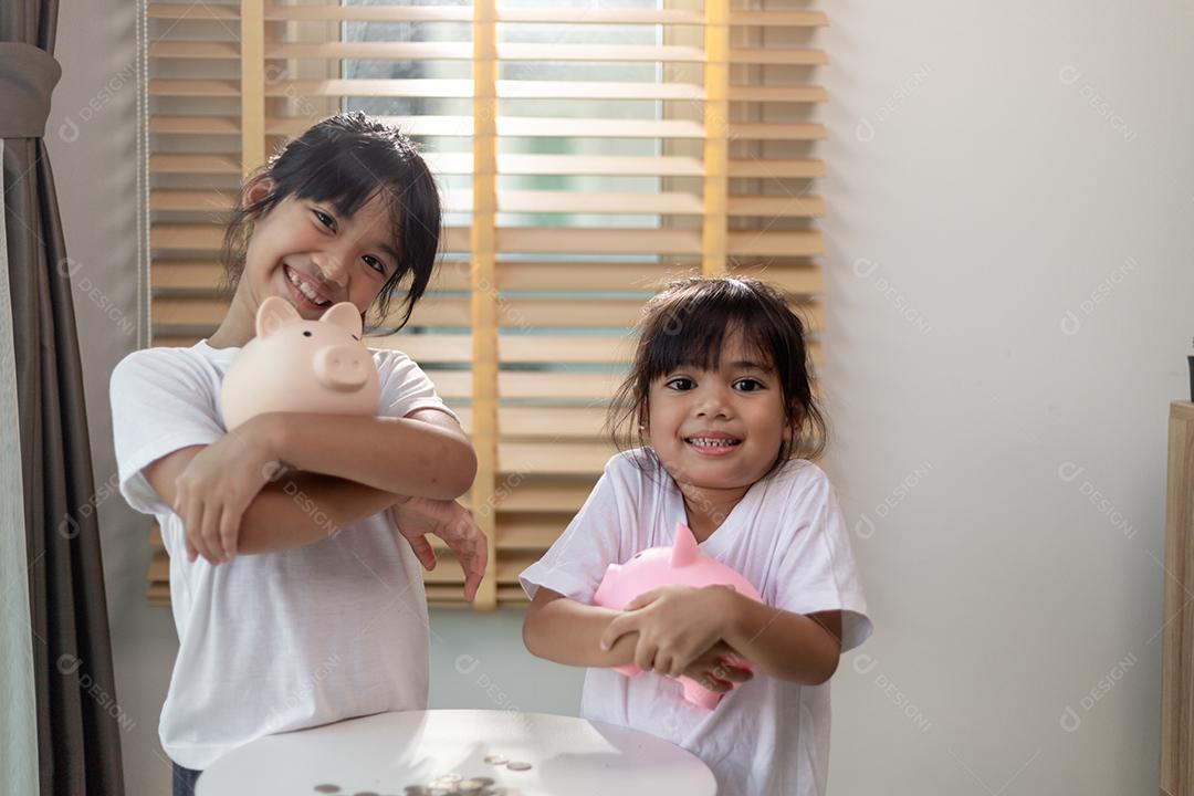 Menina asiática economizando dinheiro em um cofrinho, aprendendo sobre economia, Kid economiza dinheiro para educação futura. Conceito de dinheiro, finanças, seguros e pessoas