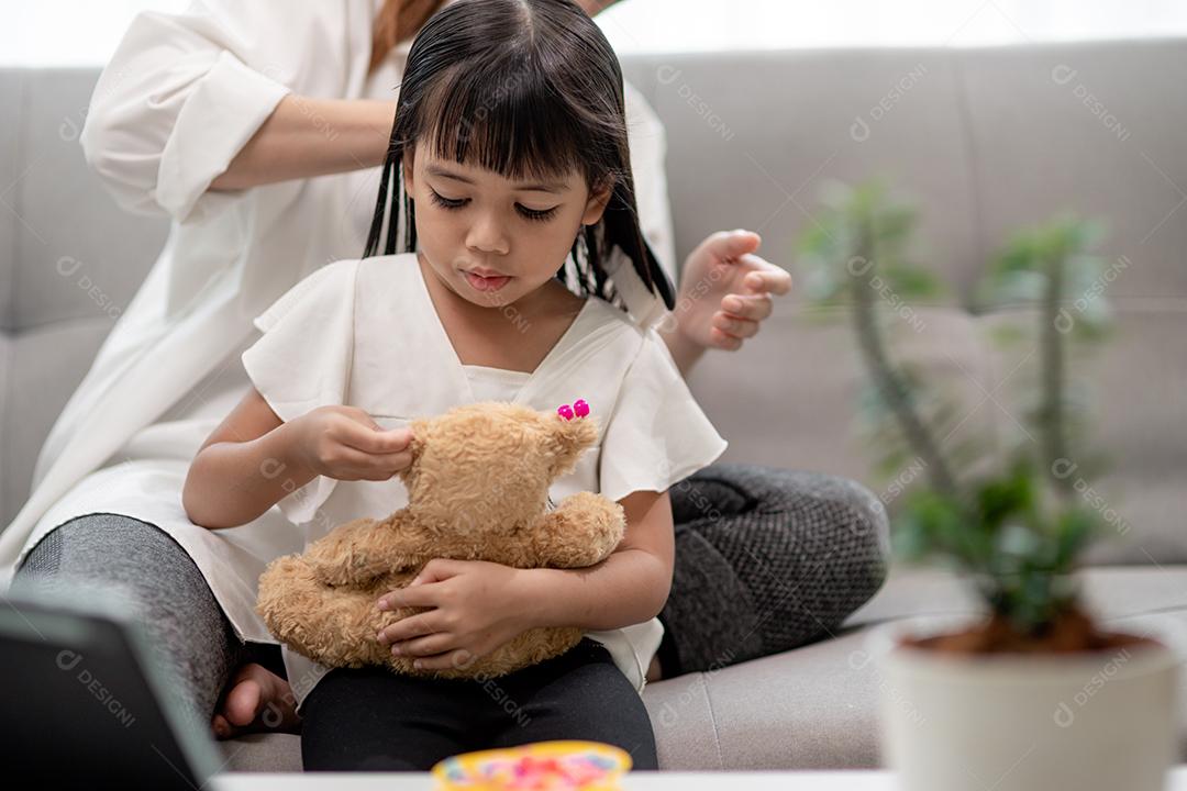 Jovem mãe asiática amarrando o cabelo da filha