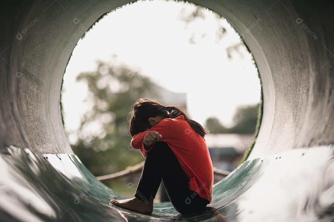 Uma garota asiática solitária sentada sozinha no parque, uma garota tailandesa triste pensa algo, conceito de garota triste