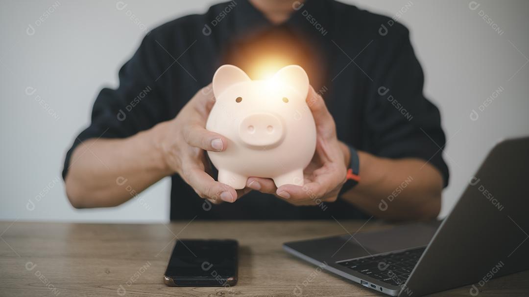 Mão de homem segurando o cofrinho na mesa de madeira, economizando dinheiro riqueza e conceito financeiro, negócios, finanças, investimento, planejamento financeiro.