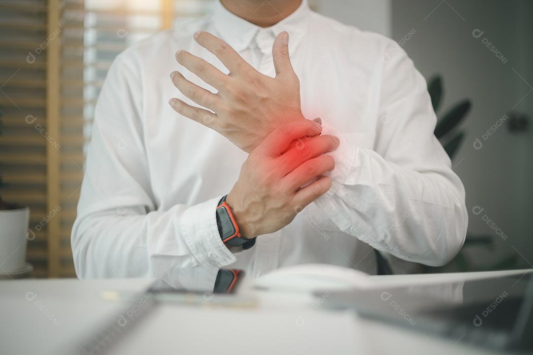 Empregado do sexo masculino sentado no local de trabalho do escritório com laptop, massageando o pulso dolorido, sofrendo de nervo comprimido, músculos rígidos, síndrome do túnel do carpo após digitar no laptop