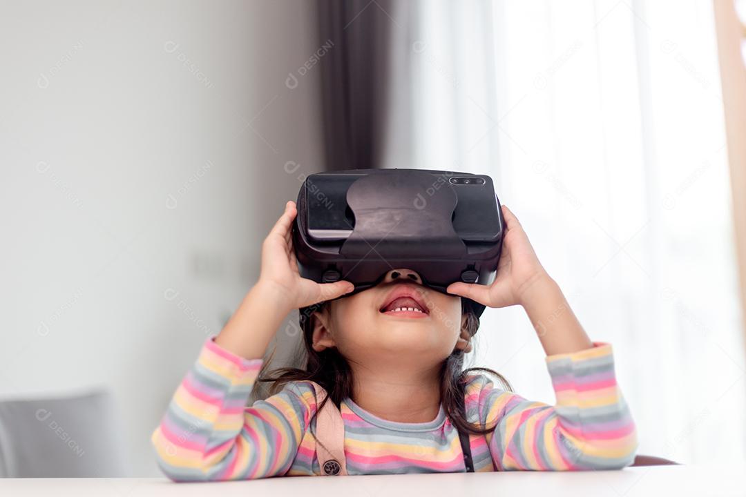 Criança com fone de ouvido de realidade virtual sentado atrás da mesa dentro de casa