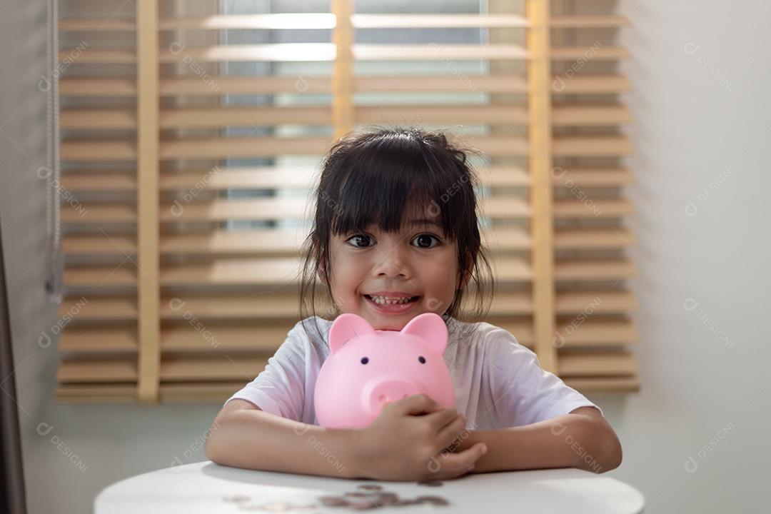 Menina asiática economizando dinheiro em um cofrinho, aprendendo sobre economia, Kid economiza dinheiro para educação futura. Conceito de dinheiro, finanças, seguros e pessoas