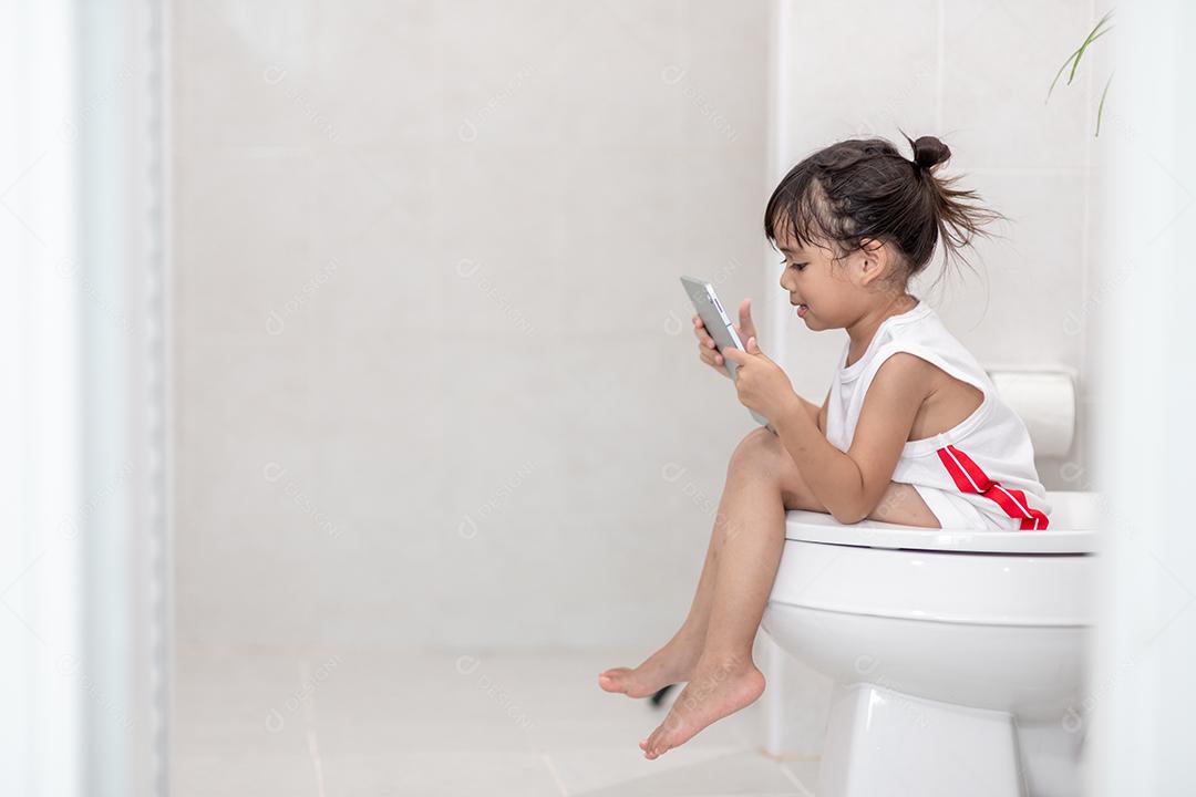 criança sentada no vaso sanitário segurando o tablet. conceito de smartphone viciado em criança