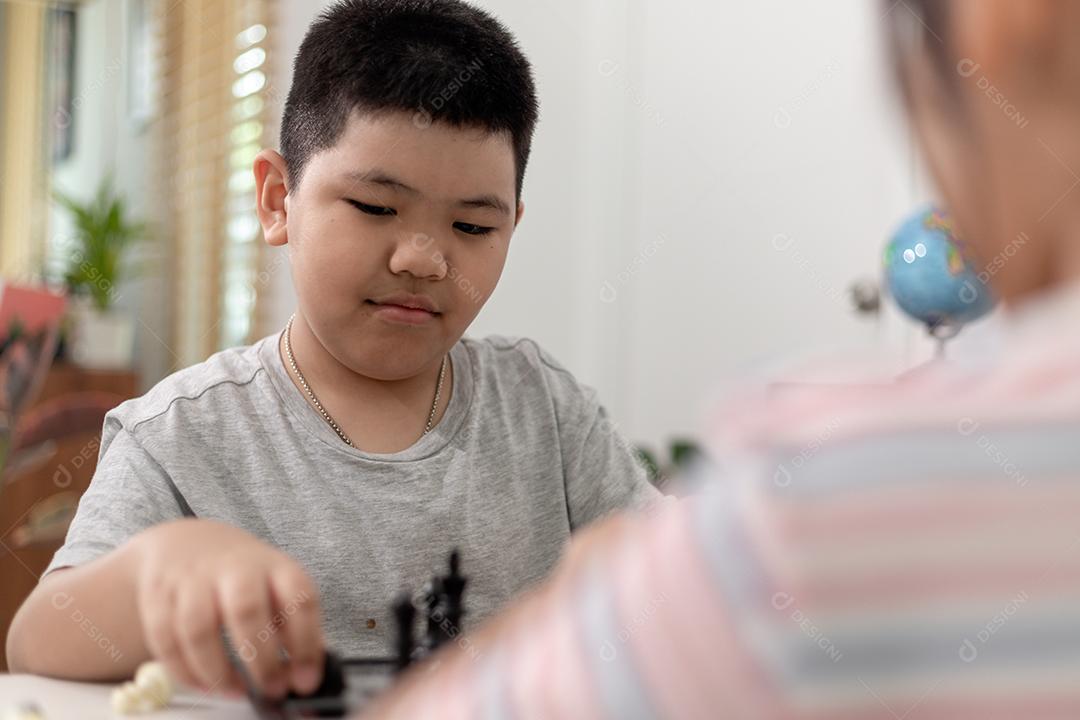 Menino e menina estão jogando xadrez em casa. Crianças jogando xadrez