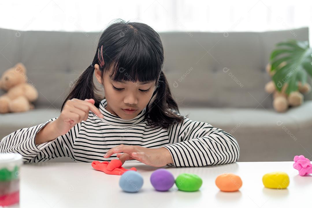 A garotinha está aprendendo a usar massinha colorida em uma sala bem iluminada