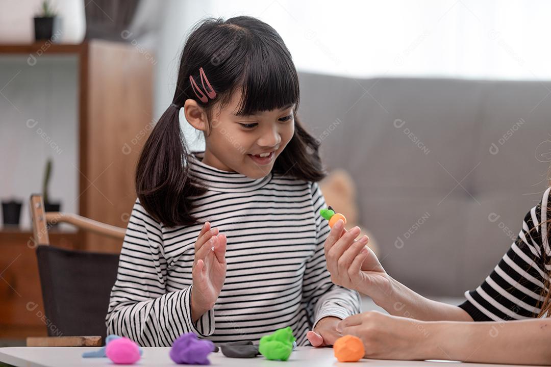 Mãe e filha asiáticas jogam massa de modelar juntas na cozinha com luz do dia e parecem felizes. Conceito de desfrutar com tempo em família