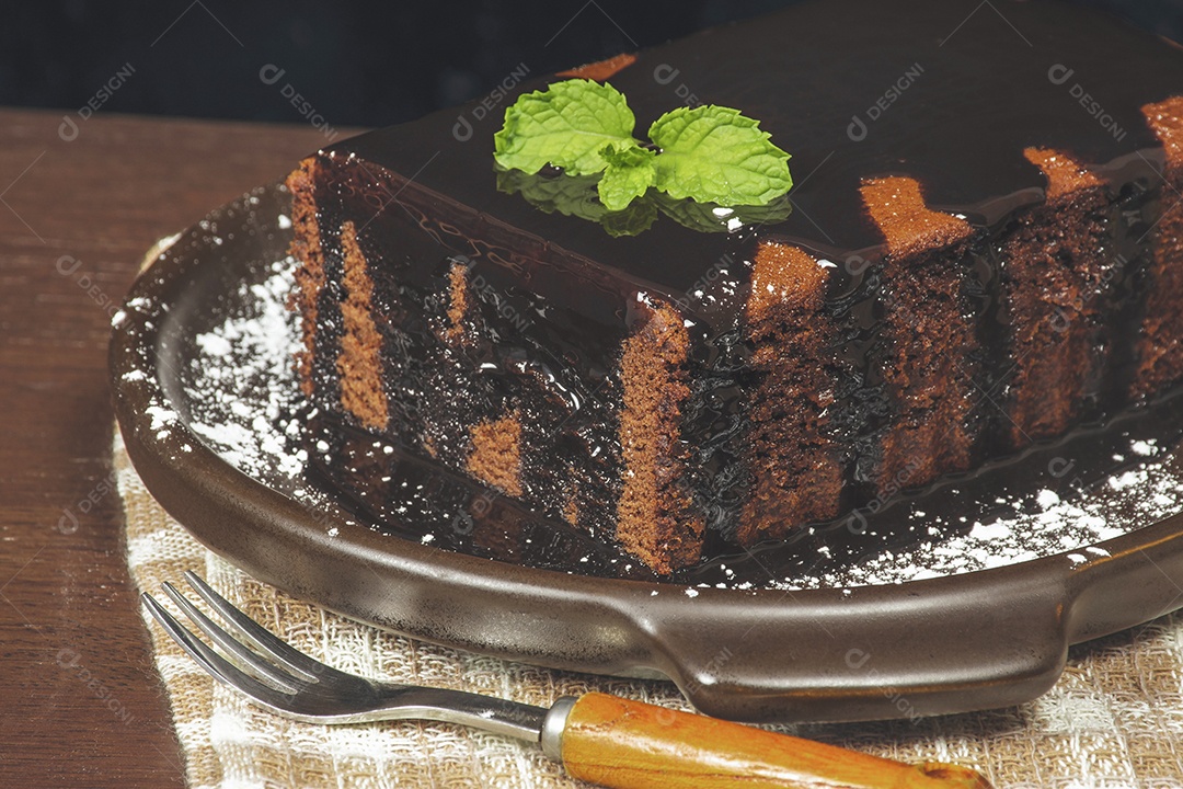 Bolo de chocolate caseiro com chocolate coberto em um prato marrom.