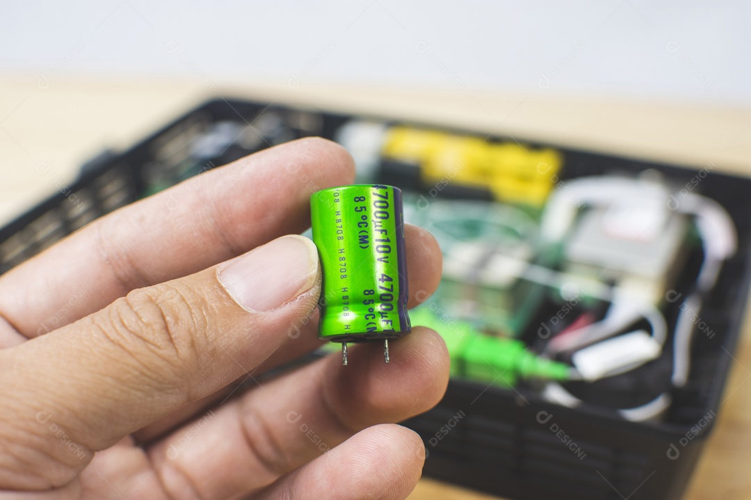 Feche o capacitor eletrolítico na mão com o pano de fundo desfocado da placa de circuito