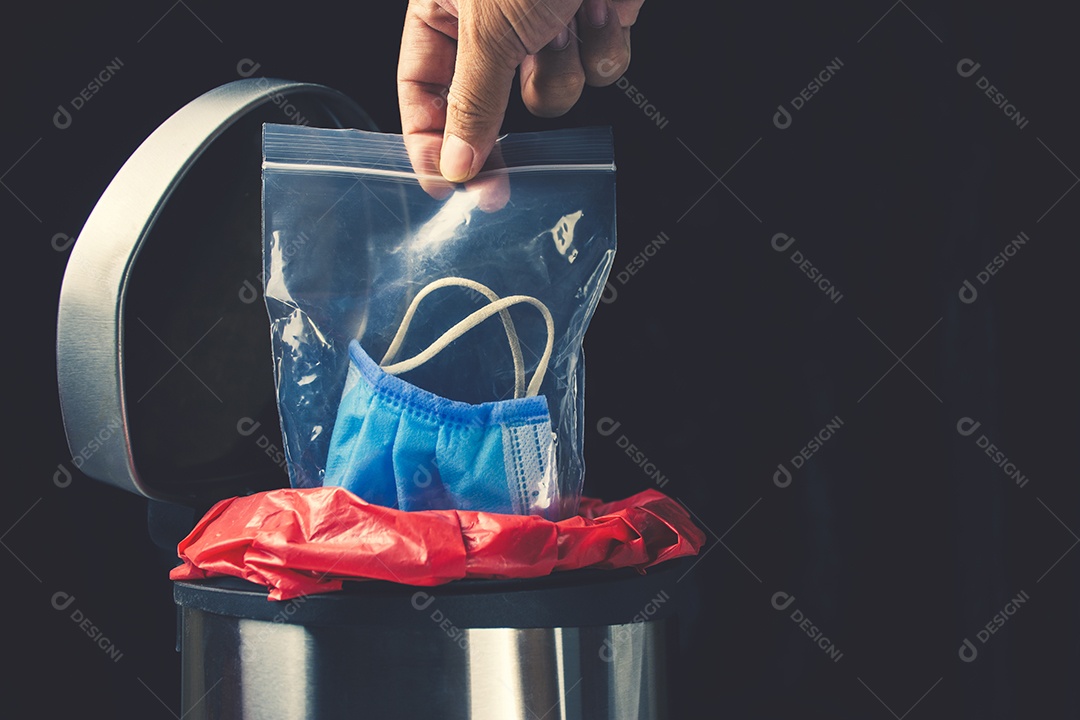 Mão deixar máscara médica descartável em saco com zíper na lixeira infectada