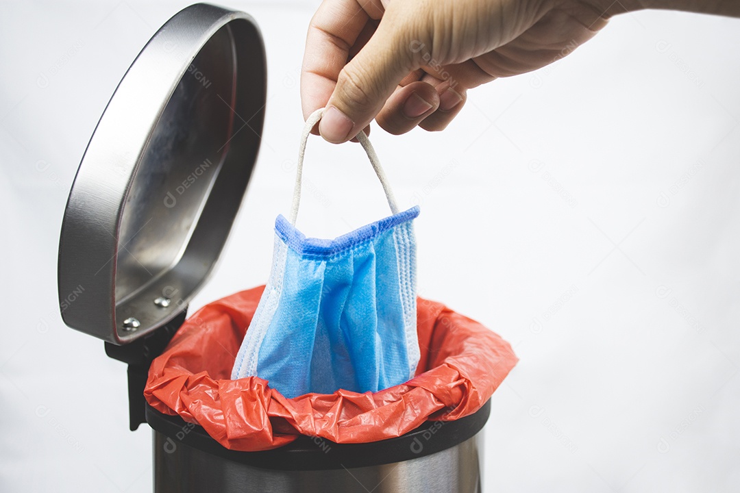 Homem jogando uma máscara facial médica para a lixeira infecciosa no fundo branco