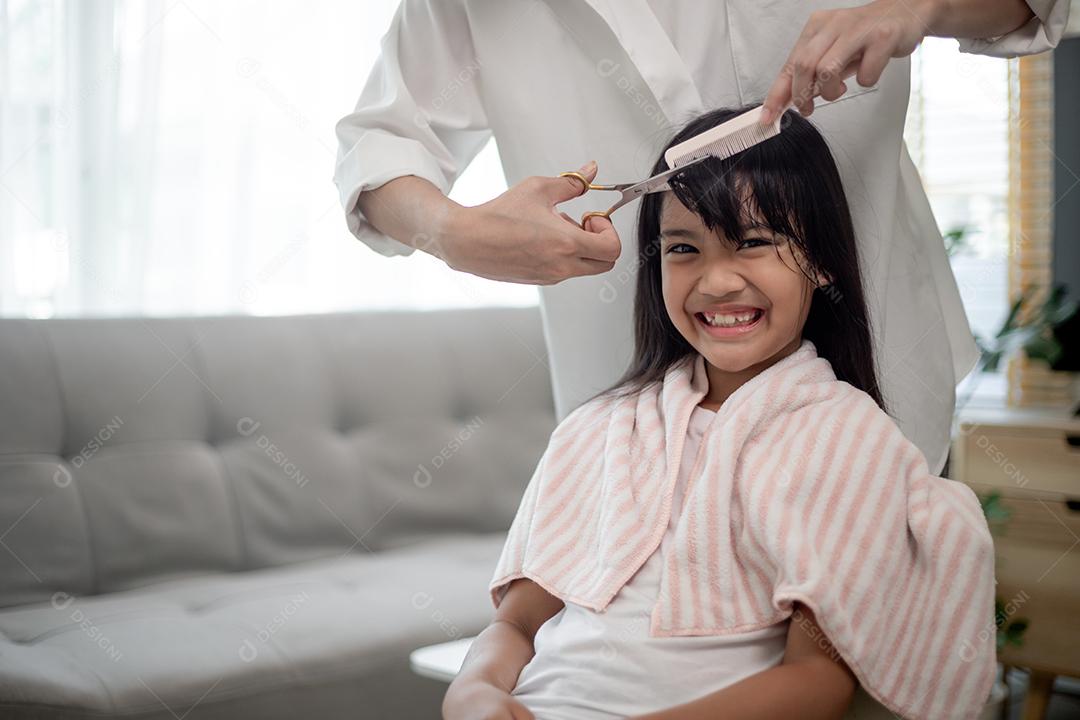 Mãe asiática cortando cabelo para sua filha na sala de estar em casa