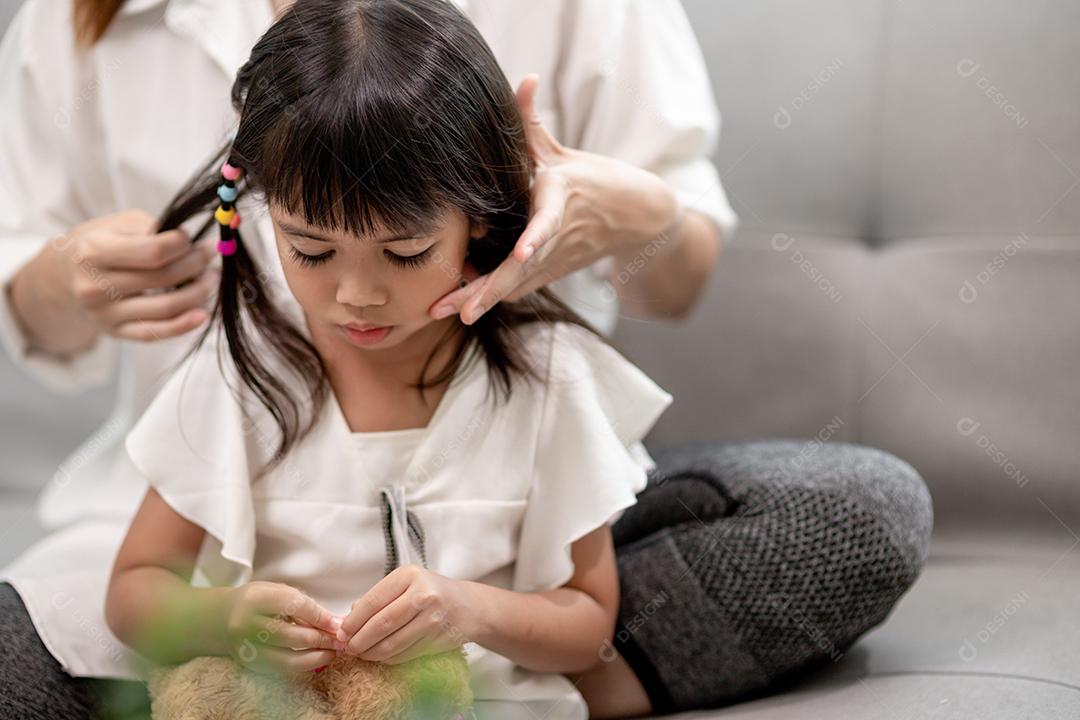 Jovem mãe asiática amarrando o cabelo da filha