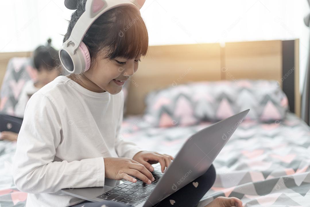 Menina asiática usando um laptop enquanto estava deitado na cama