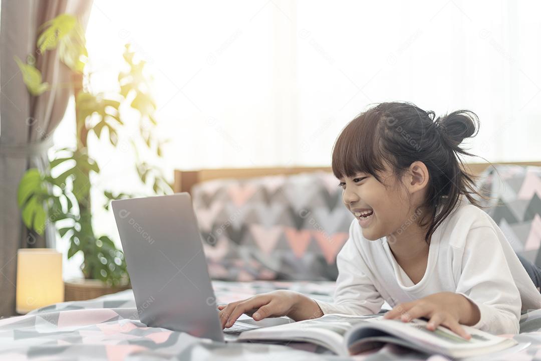 Menina asiática usando um laptop enquanto estava deitado na cama