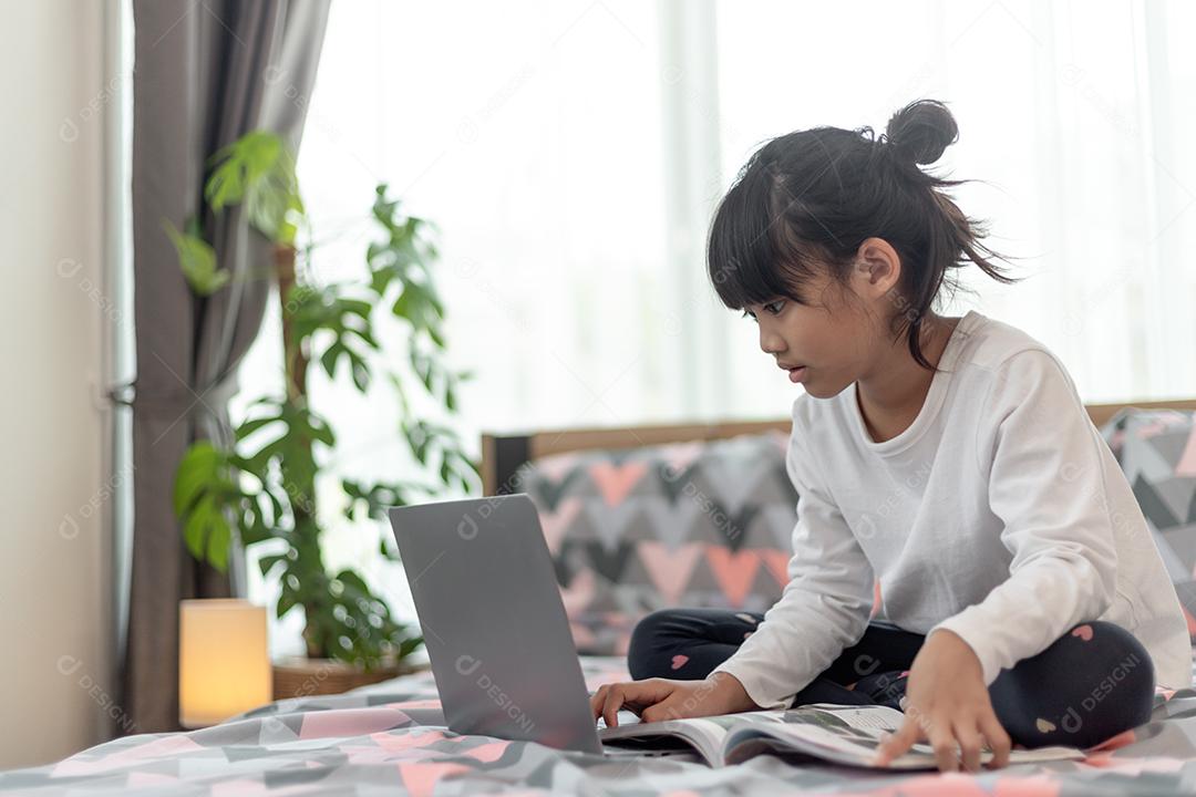 Menina asiática usando um laptop enquanto estava deitado na cama