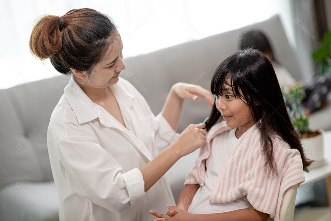 Mãe asiática cortando cabelo para a filha na sala de estar em casa enquanto fica em casa segura do Covid-19 Coronavirus durante o bloqueio. Conceito de auto-quarentena e distanciamento social.