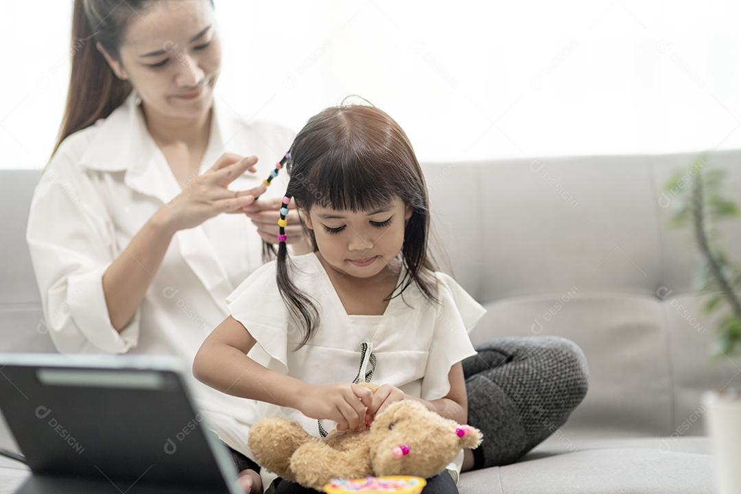 Jovem mãe asiática amarrando o cabelo da filha