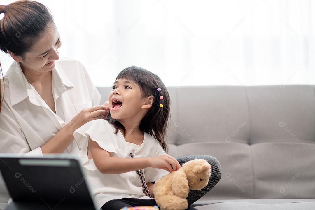 Jovem mãe asiática amarrando o cabelo da filha