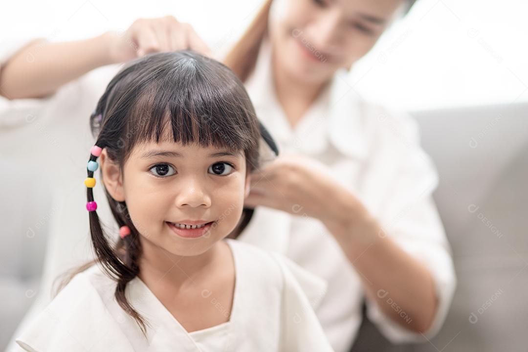 Jovem mãe asiática amarrando o cabelo da filha