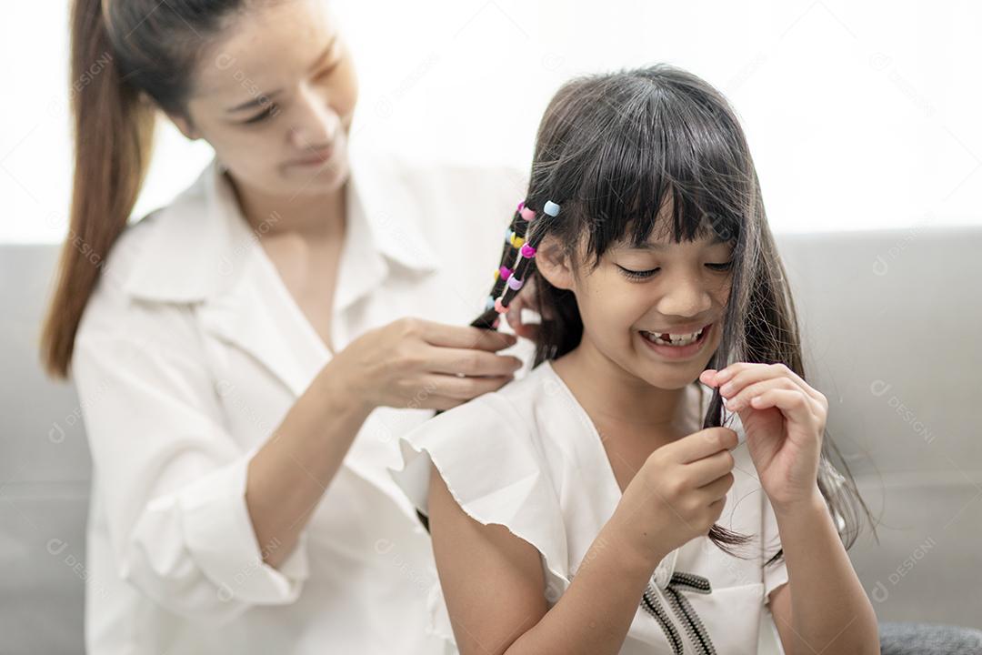 Jovem mãe asiática amarrando o cabelo da filha