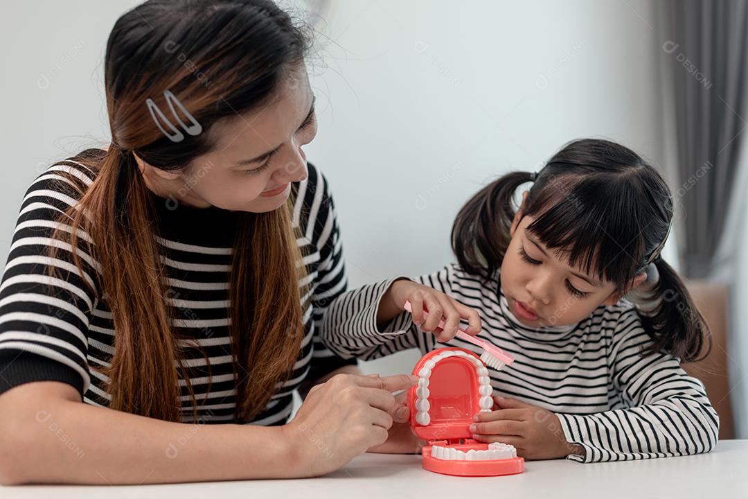 mãe ensinando filha criança escovando os dentes em casa