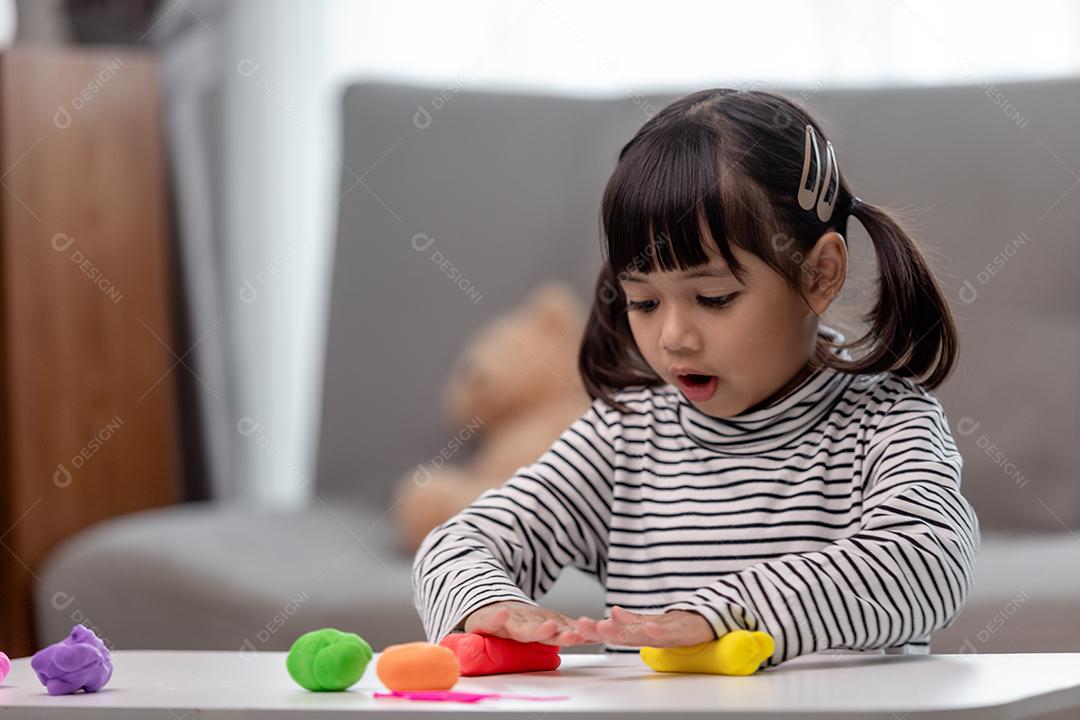 A garotinha está aprendendo a usar massinha colorida em uma sala bem iluminada