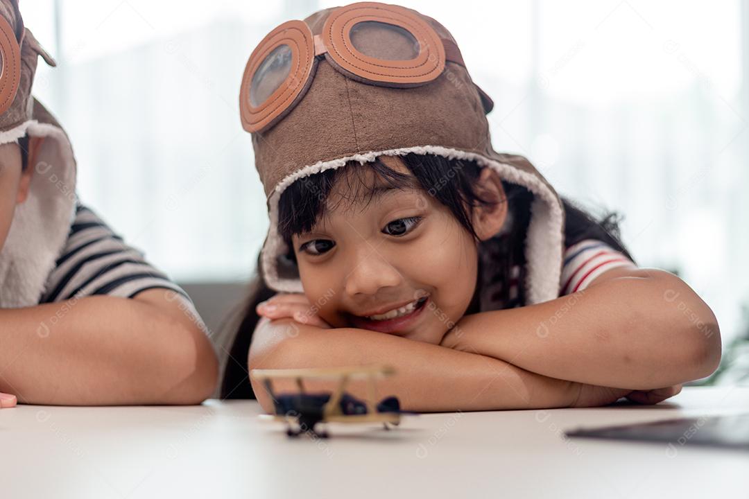 Menina asiática em casa brinca com um avião de brinquedo, ela quer se tornar piloto. Piloto sonhador.