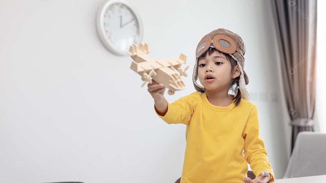 Menina asiática em casa brinca com um avião de brinquedo, ela quer se tornar piloto. Piloto sonhador.