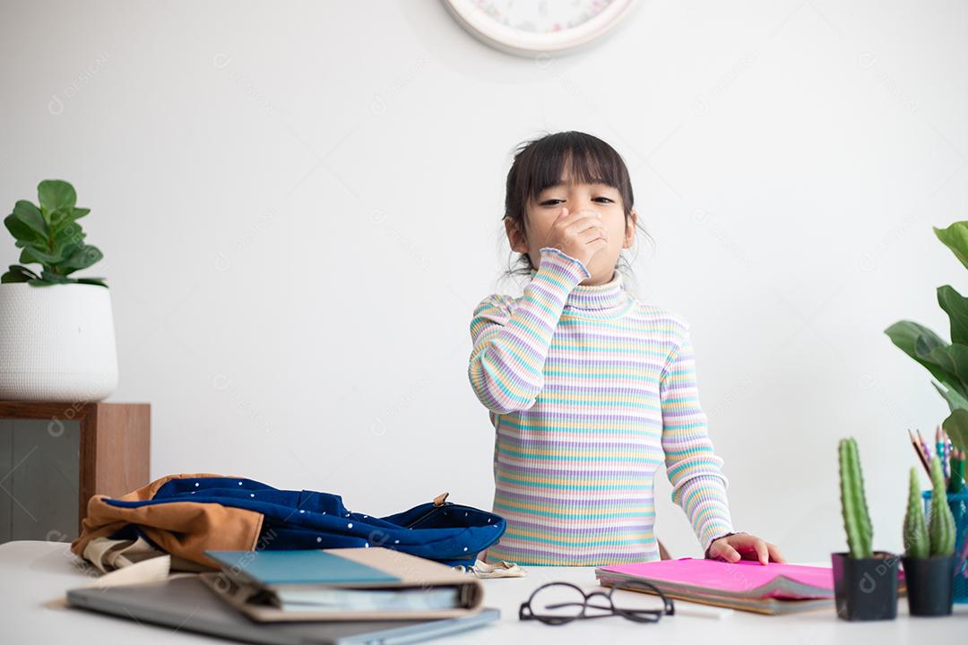 Retrato de uma menina asiática doente e insalubre com sintomas de gripe, tosse, mantendo a mão perto da boca.