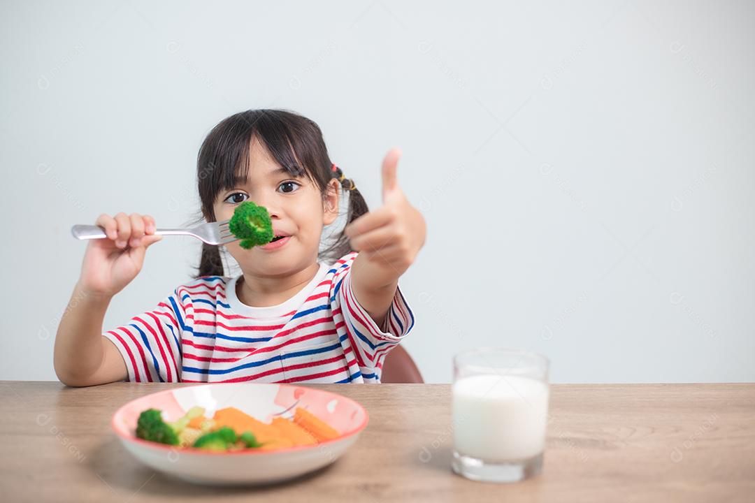 Menina asiática bonita comendo vegetais saudáveis ​​e leite para sua refeição