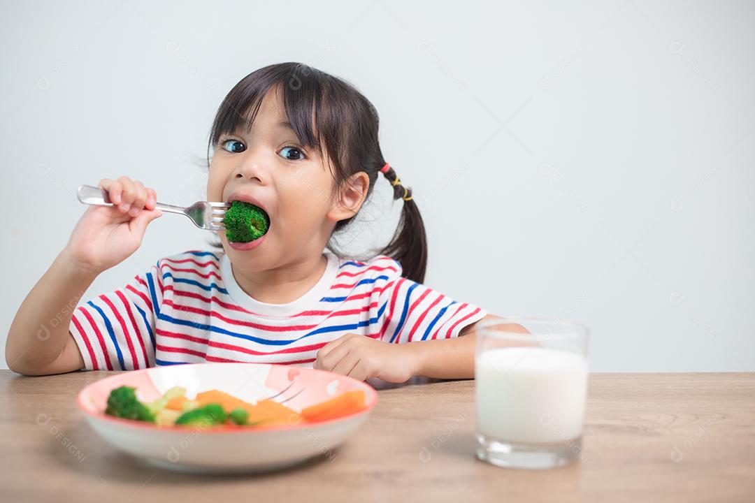 Menina asiática bonita comendo vegetais saudáveis ​​e leite para sua refeição