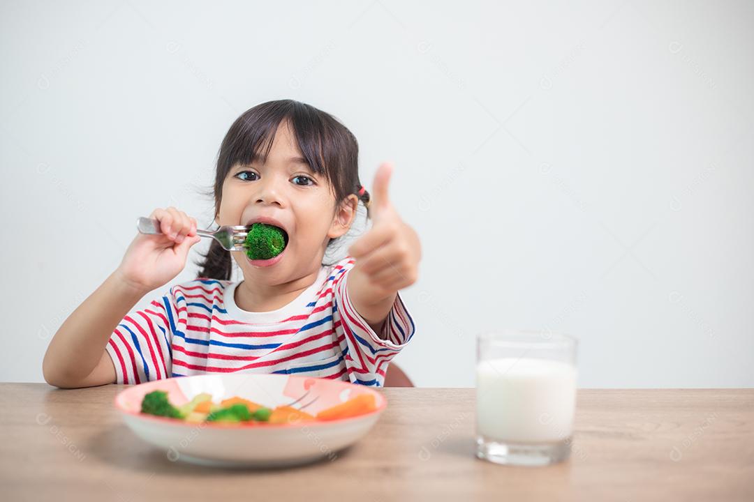 Menina asiática bonita comendo vegetais saudáveis ​​e leite para sua refeição