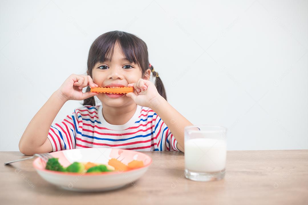 Menina asiática bonita comendo vegetais saudáveis ​​e leite para sua refeição