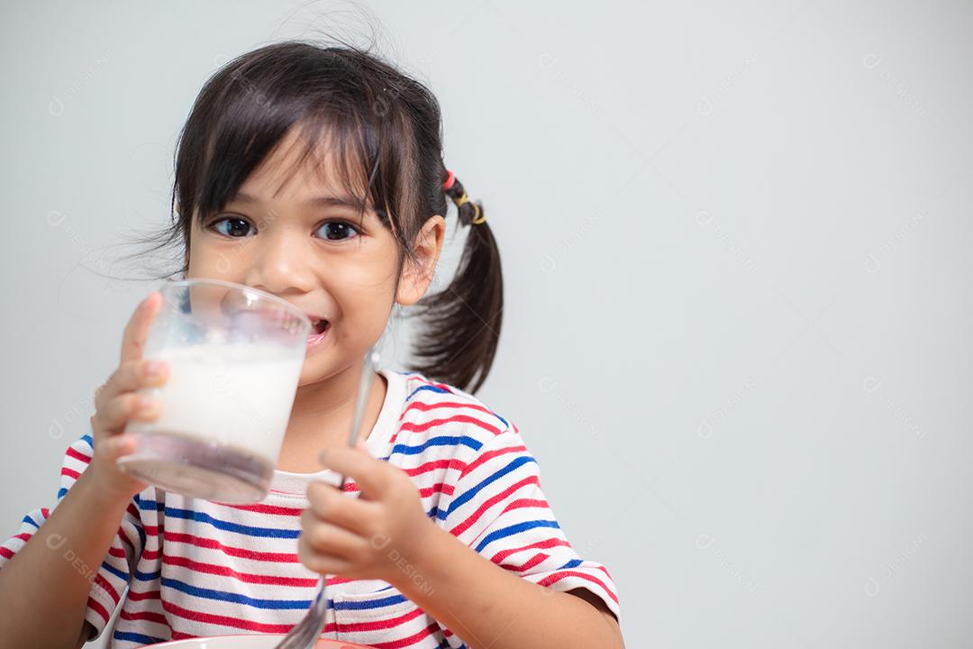 Menina asiática bonita comendo vegetais saudáveis ​​e leite para sua refeição