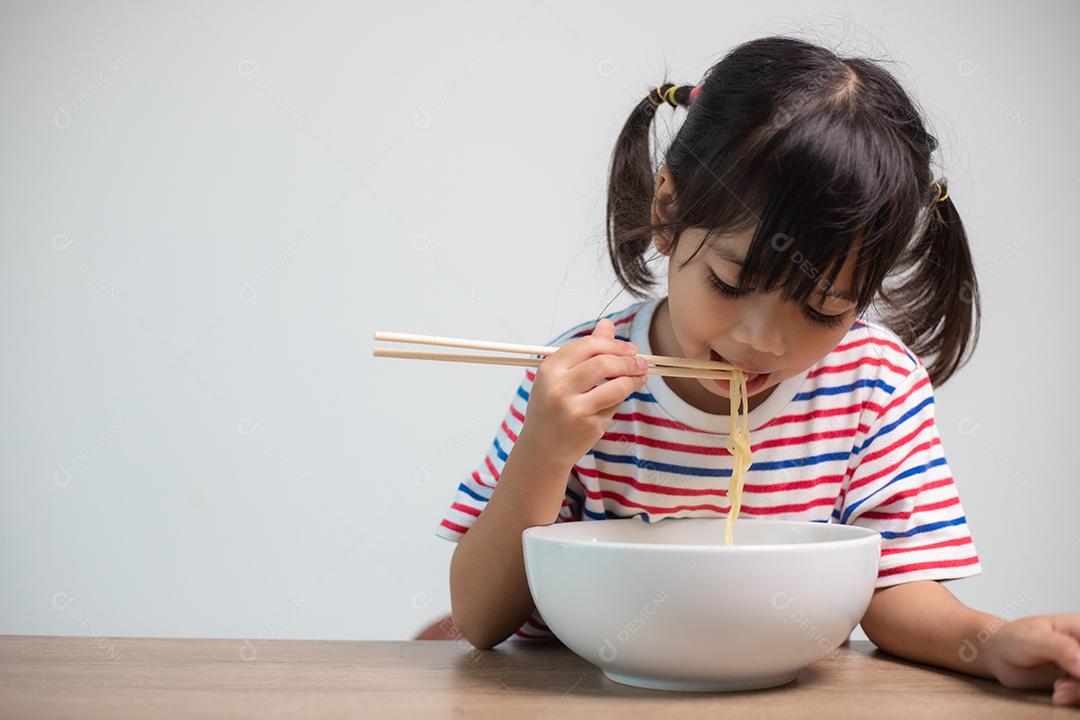 Linda garota asiática comendo deliciosos macarrão instantâneo em casa.