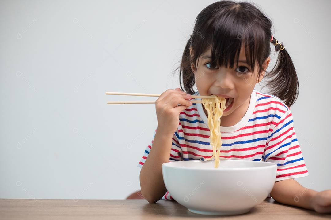 Linda garota asiática comendo deliciosos macarrão instantâneo em casa.