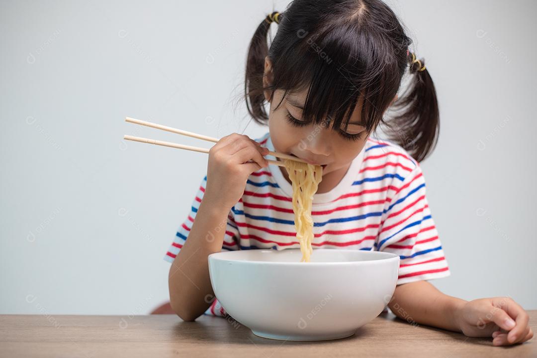Linda garota asiática comendo deliciosos macarrão instantâneo em casa.