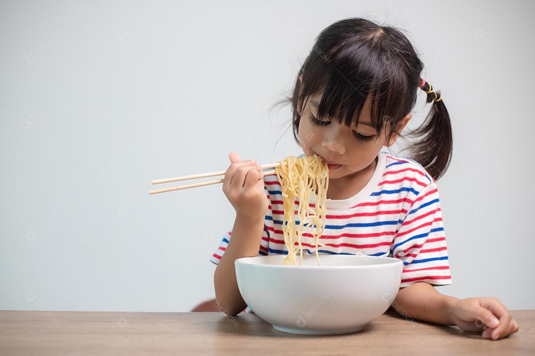 Linda garota asiática comendo deliciosos macarrão instantâneo em casa.