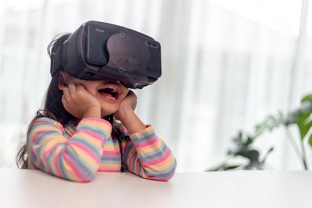 Criança com fone de ouvido de realidade virtual sentado atrás da mesa dentro de casa