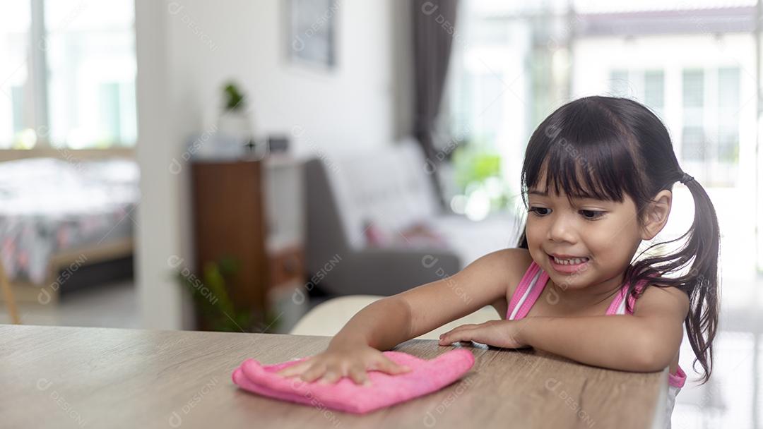 menina asiática feliz aprendendo a limpar com um pano na sala de estar em casa. trabalho doméstico e conceito doméstico.