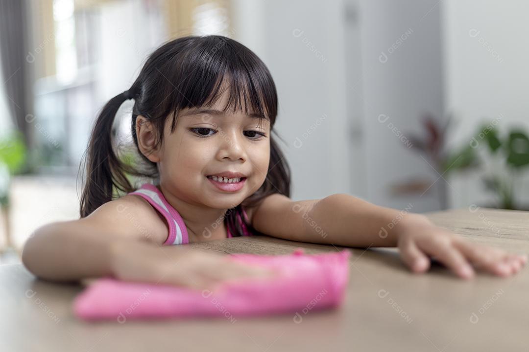 menina asiática feliz aprendendo a limpar com um pano na sala de estar em casa. trabalho doméstico e conceito doméstico.