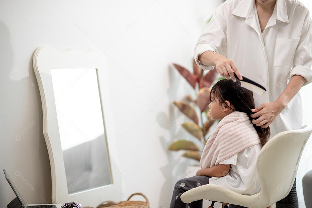 Mãe asiática cortando cabelo para a filha na sala de estar em casa enquanto fica em casa segura do Covid-19 Coronavirus durante o bloqueio. Conceito de auto-quarentena e distanciamento social.