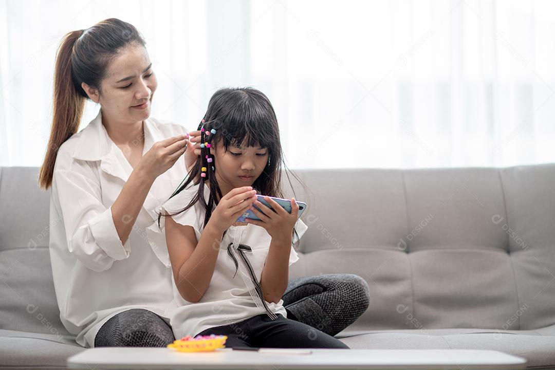 Jovem mãe asiática amarrando o cabelo da filha