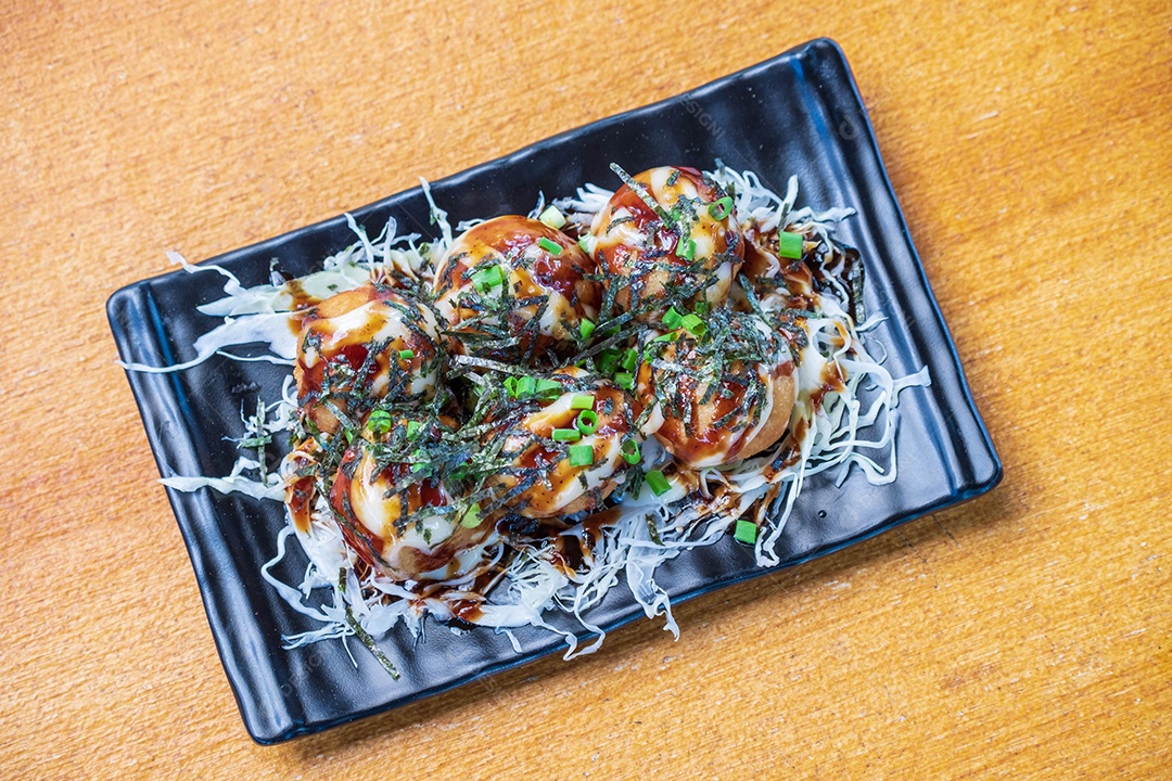 Filé de Polvo Takoyaki Decore com alga. repolho branco picado e cebolinha em um prato preto, Saimoden, circulado em uma mesa de madeira