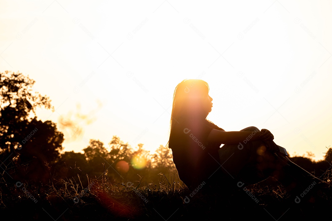 Mulher de silhueta sentada no chão durante o pôr do sol, fundo atmosférico laranja.