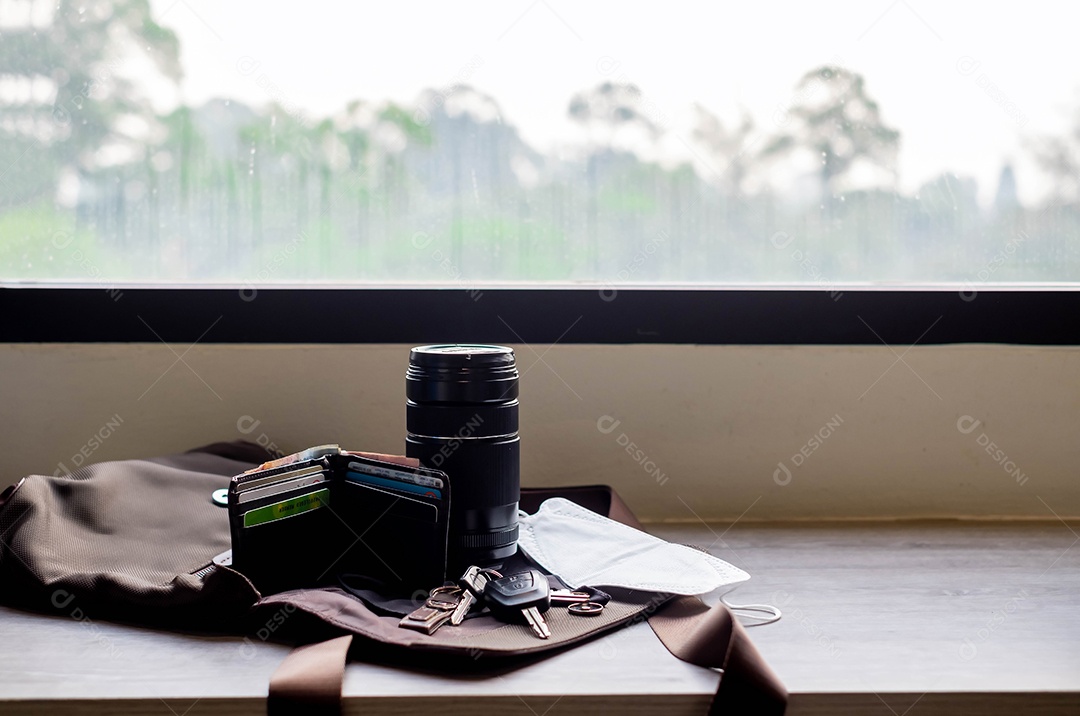 Equipamento de viagem na era epidêmica do Covid-19 perto das janelas, bolsas, lentes de câmera, chaveiros de carro, máscaras, carteira