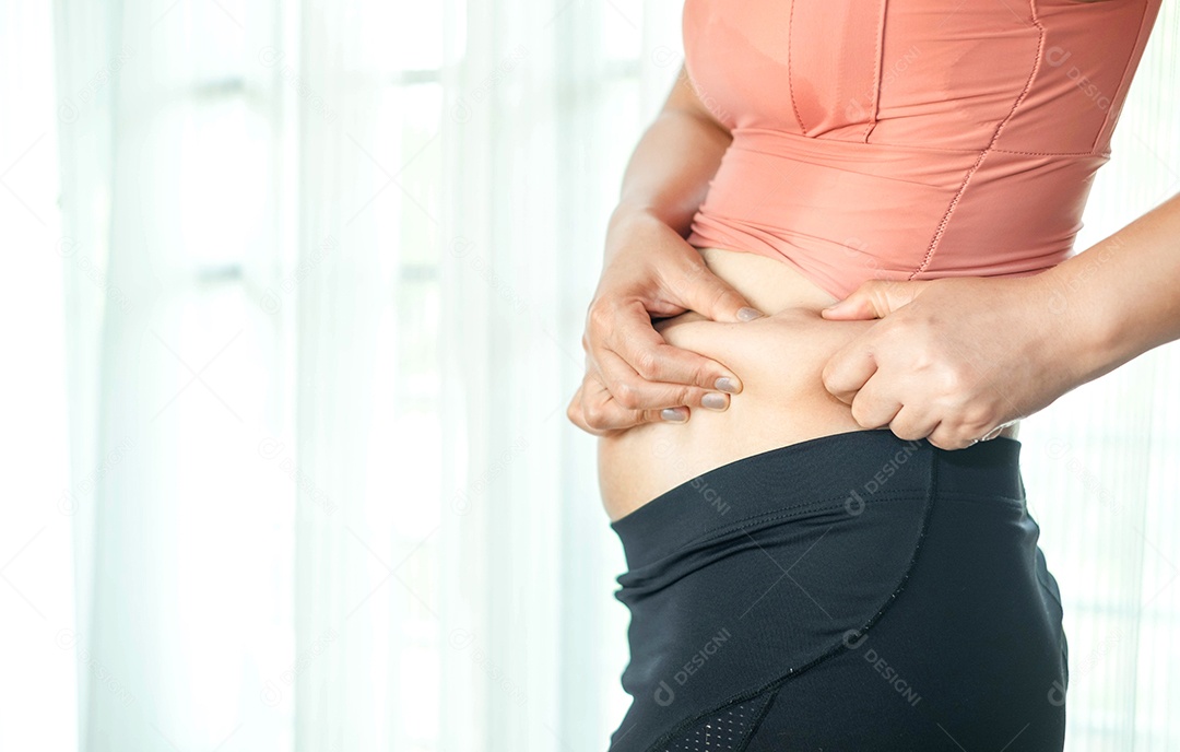 Conceito de cuidados com o corpo: a mão da mulher beliscando o excesso de gordura da barriga, corpo de mulher gorda e insalubre